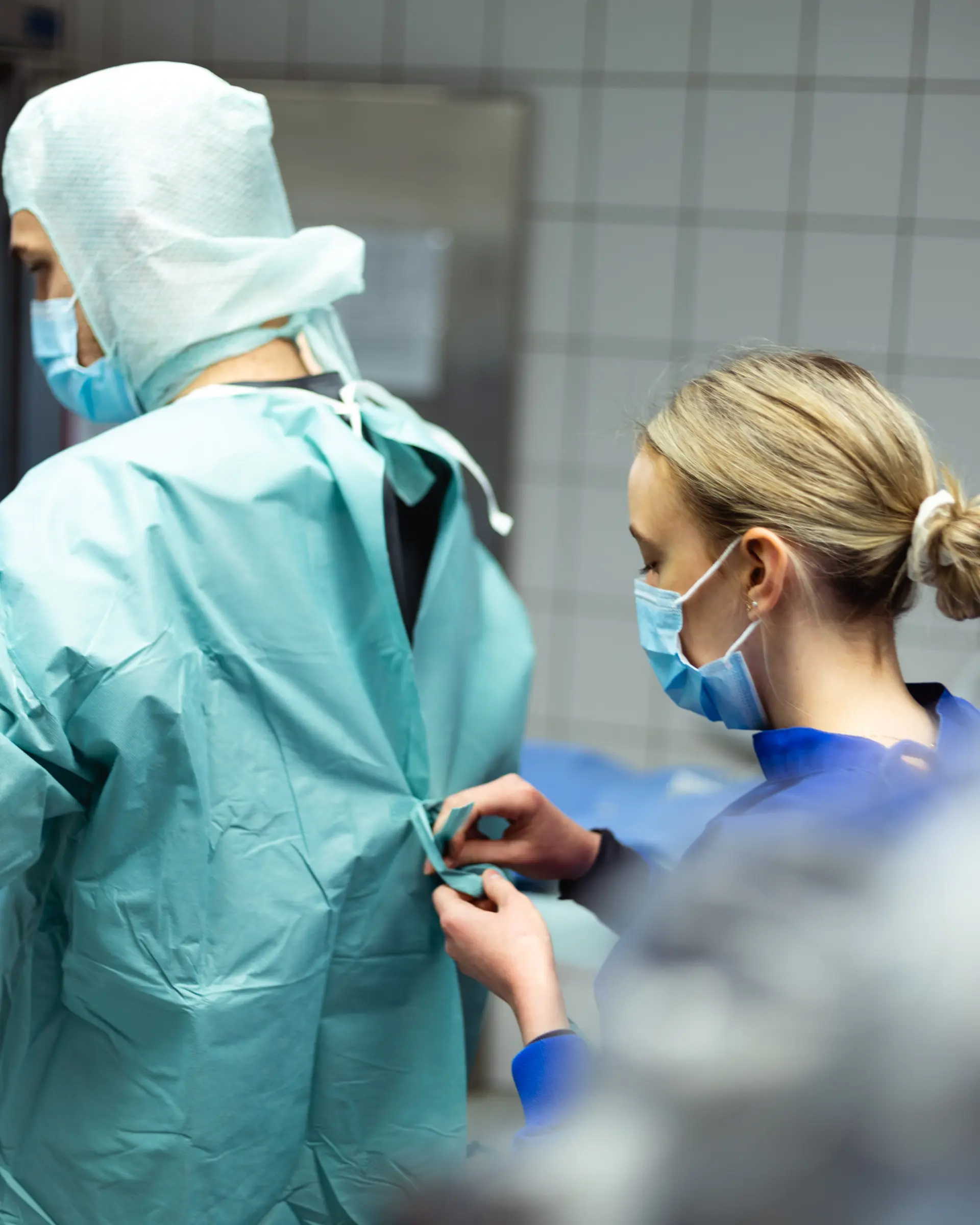 Mitarbeiterin unterstützt einen Arzt beim Anlegen der sterilen OP-Kleidung